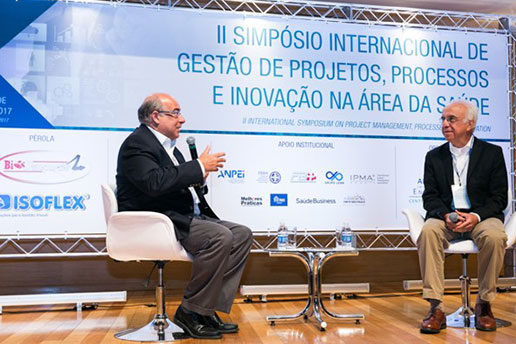 Registro de dois convidados, sentados e enquanto falam, durante o II Simpósio Internacional.